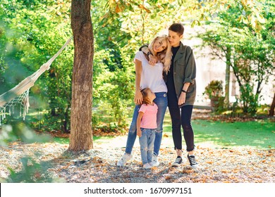 Lesbian Parents And Their Adopted Daughter In The Backyard On A Sunny Day. LGBT Parenting And Child's Mental Health.