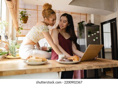 Lesbian Women Couple In The Kitchen At Home With Computer, Multiracial Women Who Love Each Other And Live Together.