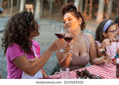 lesbian women toasting red wine on picnic table – lesbian couple relax toast with drink glasses – happy girls friends sibling clinking glasses  - Powered by Shutterstock