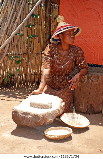 LESEDI,SOUTH AFRICA - JAN 1:Sotho woman in\
handmade dress and conical hat cooking maize meal at tribal house\
on January 1,2008 at Lesedi Village, South Africa.Maize meal is\
basic African\
ingredient.
