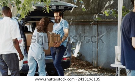 Less fortunate caucasian woman and african american man are seen accepting donation box from male volunteer at a food drive. Charity worker distributes essentials to the needy and homeless people.