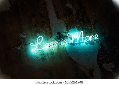 Less Is More Sign Made Of Green Blue Led Neon Tube Lights. Dark Grunge Textured Wall. Motivational Minimalist Quotation