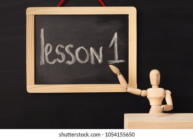 Lesson 1 written with chalk on blackboard. Wooden mannequin sitting at teacher's table in classroom. Mockup for online educational units. - Powered by Shutterstock