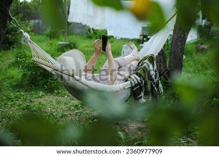 A Lesson in Self-Care: Woman in Wide-Brim Hat Unplugs Yet Stays Connected, Lounging in Her Hammock Sanctuary