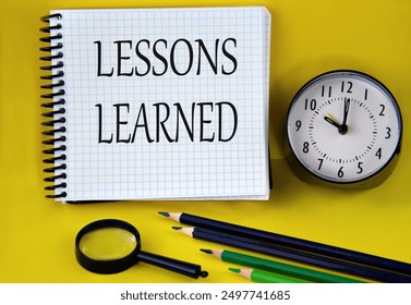 LESSONS LEARNED - words in a white notebook with an alarm clock, pencils and magnifying glass in the background