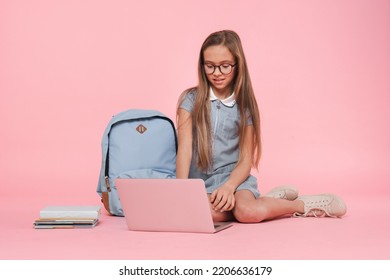 Lessons tutoring online. Happy caucasian young preteen schoolgirl teenage girl in uniform with bag using laptop e-learning remote studying education isolated in pink