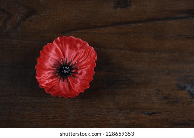 Lest We Forget, Red Flanders Poppy Lapel Pin Badge For November 11, Remembrance Day Appeal, On Dark Recycled Wood Background, With Copy Space.