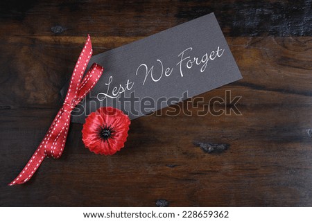 Lest We Forget, Red Flanders Poppy Lapel Pin Badge for November 11, Remembrance Day appeal, on dark recycled wood background.