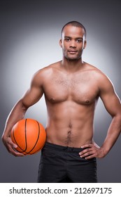 Let the game begin. Young shirtless African man holding basketball ball and looking at camera while standing against grey background