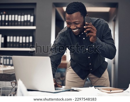 Let me quickly make note of that...a handsome young male architect taking a phonecall while working on a laptop in a modern office.