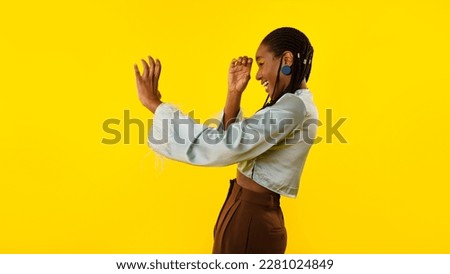Let Me See. Excited African American Woman Pretending Watching Through Spyglass Holding Invisible Telescope In Hands And Looking Aside Posing In Studio Over Yellow Background. Panorama, Side View