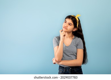 Let Me Think. Doubtful Indian Teen Girl Looking Upwards At Copy Space, Posing On Blue Studio Background. Thoughtful Adolescent Dreaming, Imagining Something, Creating Idea