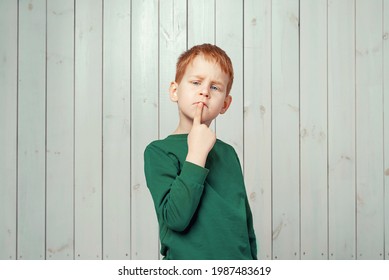 Let me think. Ginger little boy 7-9 years old looking sideways with doubtful and skeptical expression, standing against wooden background - Shutterstock ID 1987483619