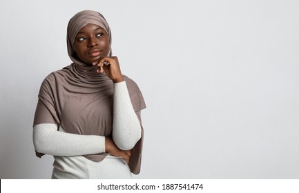 Let Me Think. Pensive Black Muslim Woman In Hijab Looking At Copy Space With Interest, African Islamic Lady In Headscarf Thinking About Offer Or Deal, Standing Over Light Studio Background, Panorama