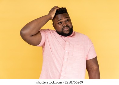 Let me think. Portrait of pensive man wearing pink shirt holding hand on head and thinking, pondering idea, looking away with thoughtful expression. Indoor studio shot isolated on yellow background. - Shutterstock ID 2258755269