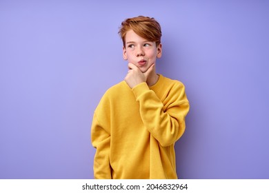 Lass mich nachdenken. Umsichtiger, cleverer Rotkopfschüler in gelbem Hemd mit verwirrtem ernsthaften Ausdruck, kinderdenkend, wählerisch. Studioaufnahme einzeln auf violettem Hintergrund
