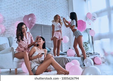 Let the party begin! Four attractive young women in pajamas pampering themselves while having a slumber party in the bedroom with balloons all over the place