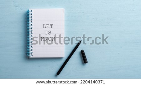 Let us know sign written in spiral notebook with a black marker next to it placed on blue wooden background.