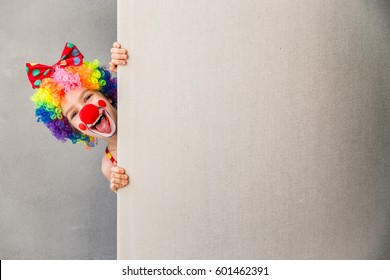 Давайте отпразднуем! Забавный ребенок клоун прячется за картонным пустым. Ребенок держит баннер с копировальным пространством для вашего текста. 1 апреля Дурак день концепции