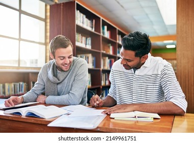 Lets compare notes. Shot of two university students working together in the library at campus.