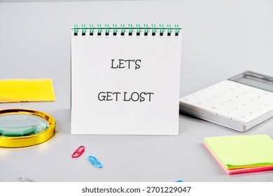 Lets Get Lost notepad on a grey desk. Magnifier, calculator, and sticky notes hint at discovery and uncharted territories.
