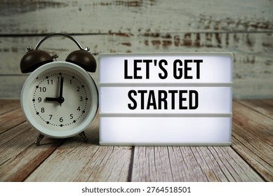 Let's Get Started text on light box with alarm clock on wooden background