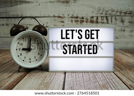 Let's Get Started text on light box with alarm clock on wooden background