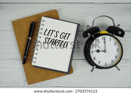 Let's Get Started text written on notepad with alarm clock on wooden background