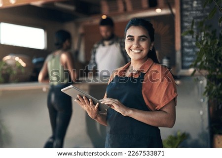 Lets get you seated. Shot of an attractive young woman standing outside her restaurant and using a digital tablet.