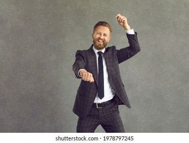 Let's Have A Party. Studio Portrait Of Goofy Young Man In Suit Dancing And Having Fun. Funny Overjoyed Businessman With Happy Positive Smile Doing Gangnam Style Move Isolated On Grey Background