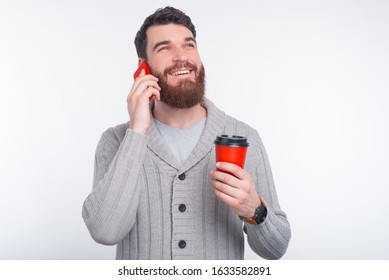 Let's have a talk and a coffee break. Smiling man is having a conversation on his phone and holding a red cup to go.