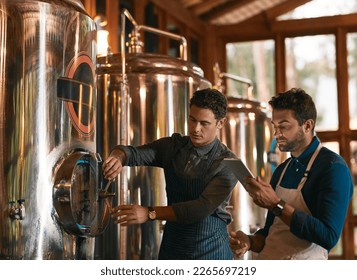 Lets hope this batch is a good one. Shot of two young working men doing inspection of their beer making machinery inside of a beer brewery during the day.