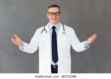 Lets Hug! Mature Male Doctor Stretching Out His Arms For Hug And Looking At Camera With Smile While Standing Against Grey Background