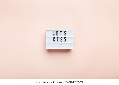 Let's kiss. Motivational quote in letter board on pink background. Top view, central composition. Romantic background for Valentine's day.