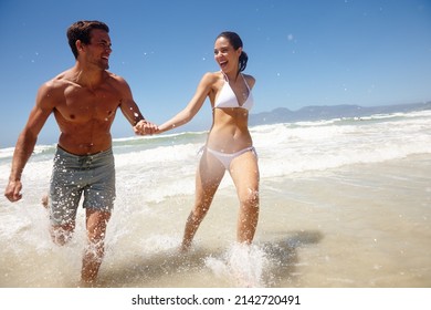 Lets paint this beach red. Shot of a playful couple running through the water at the beach. - Powered by Shutterstock