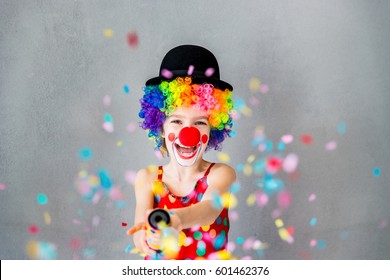 Let's party!! Funny kid clown playing at home. Child shooting party popper confetti. 1 April Fool's day concept