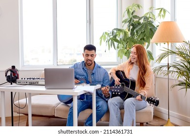 Let's Play Song Together. Friendly Female Student And Handsome Male Teacher Playing Acoustic Guitar Together During Music Lessons, Sitting On Couch In Bright Cozy Studio Room, Using Laptop