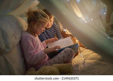 Lets read another one before bedtime. Cropped shot of siblings reading a story under a blanket fort at home. - Powered by Shutterstock