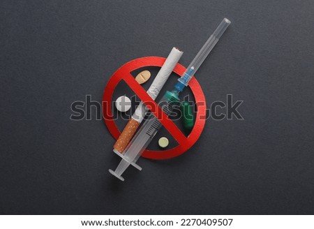 Let's stop drug addiction. Syringe and cigarette, pills with prohibition sign on dark background