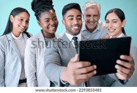Lets take a few more. Studio shot of a diverse group of corporate businesspeople using a tablet to take selfies against a blue background.