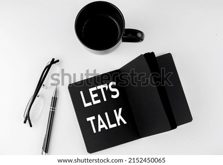 LET'S TALK written text in small black notebook with coffee , pen and glasess on a white background. Black-white style