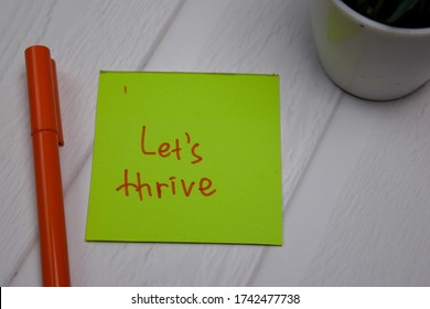 Let's Thrive write on sticky note isolated on wooden table.