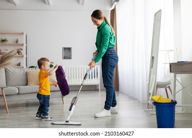 Let's Tidy Up Together. Mother And Kid Son Do The Cleaning In The House. Little Boy Helping Mom, Giving Her A Rug While Woman Wash The Floor With Mop