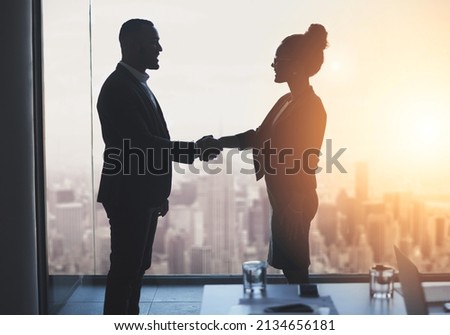 Lets work towards realizing our big ambitions together. Silhouetted shot of two businesspeople shaking hands in an office.