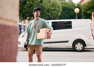 A Letter Carrier Holds Boxes During A Delivery With A Van In The Background