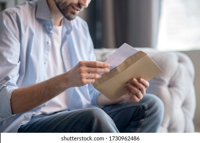 Letter. Hands of a man sitting on a sofa, slowly pulling out a letter from a paper envelope - Shutterstock ID 1730962486