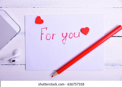 Letter with an inscription in red pencil for you, next to a mobile phone, a white wooden surface - Powered by Shutterstock