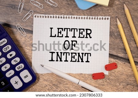 LETTER OF INTENT text on a paper clipboard with magnifier and keyboard on wooden background.