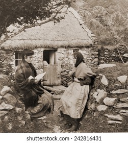 A LETTER FROM PAT IN AMERICA. Young Irish woman reading a letter from a relative in America to an older woman outside of a thatch-roofed stone cottage.