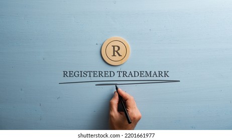 Letter R cut into wooden cut circle and male hand writing a Registered trademark sign under it. Over pastel blue wooden background. - Shutterstock ID 2201661977